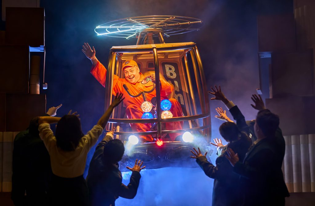 Photo of a male cast member flying in a helicopter while the rest of the cast wave goodbye